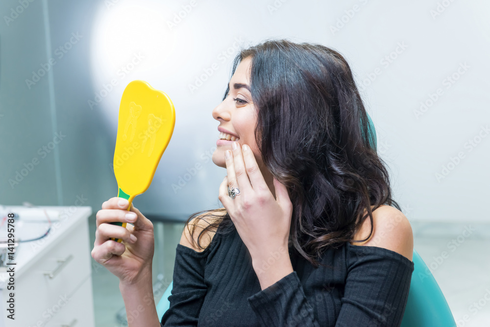 Female checking teeth in mirror. Smiling woman at dentist office. Smile wider and be beautiful. Female checking teeth in mirror. Smiling woman at dentist office. Smile wider and be beautiful.