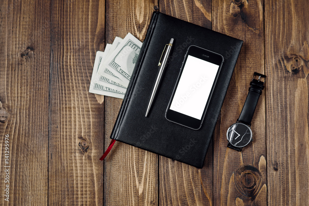Business Concept - Top view of smartphone, watch, pen, notebook and money on wooden background. Business Concept - Top view of smartphone, watch, pen, notebook and money on wooden background.