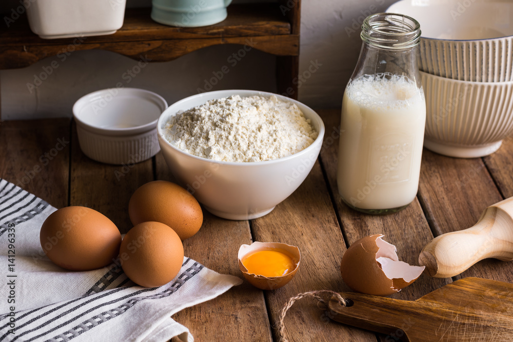 Traditional baking ingredients flour milk organic eggs on wood kitchen table in rustic rural interior, utensils, authentic style Traditional baking ingredients flour milk organic eggs on wood kitchen table in rustic rural interior, utensils, authentic style