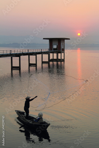 Silhouette of fishermen using nets to catch fish at the Bangpra lake with beautiful scenery of nature during sunrise time. Bang Pra Reservoir at Chonburi province in Thailand photo