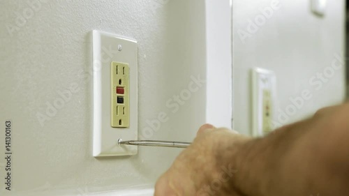 An electrician or homeowner handyman type removing the outlet cover to a ground fault outlet. photo