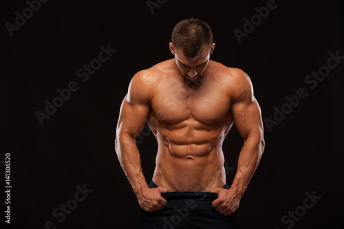 Strong Athletic Man - Fitness Model showing Torso with six pack abs. stands straight and puts his hands in trousers. isolated on black background with copyspace © satyrenko