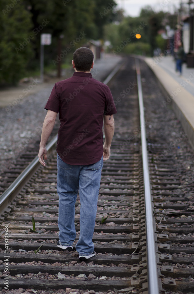 Young man walking alone on the train tracks Stock Photo | Adobe Stock