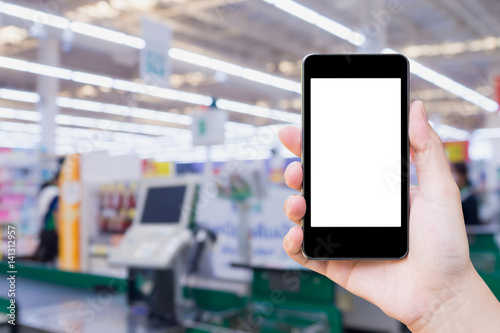 Woman hand holding mobile phone at supermarket checkout background