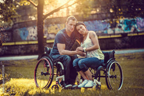 Handicapped couple in wheelchair resting in a spring park on sunset.