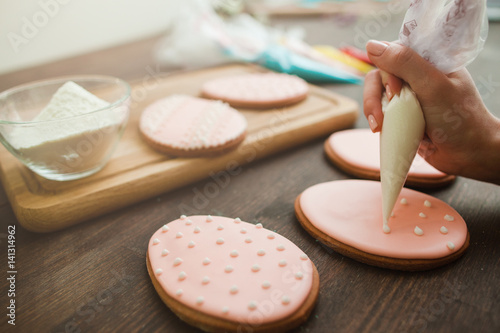 Homemade sweets and desserts. Decorating pink cookies with white icing on rustic wooden table closeup