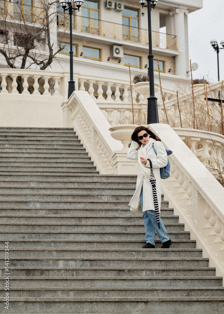 Young woman in a white coat with an umbrella down the stairs.