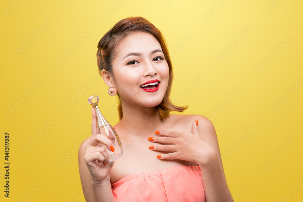 Cheerful beautiful asian young woman with charming smile holding perfume over yellow background. Cheerful beautiful asian young woman with charming smile holding perfume over yellow background.