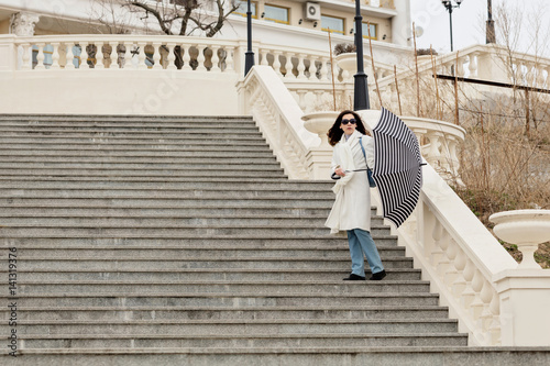 Young woman in a white coat with an umbrella down the stairs.