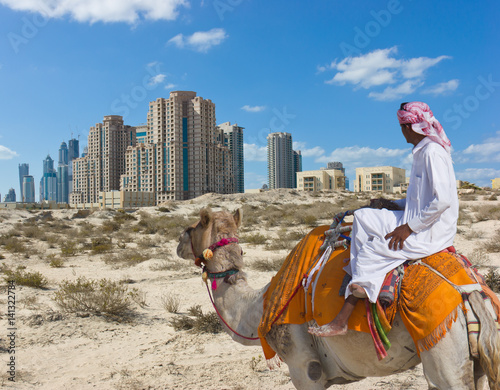 Bedouin on a camel in the desert and a modern city on the horizon