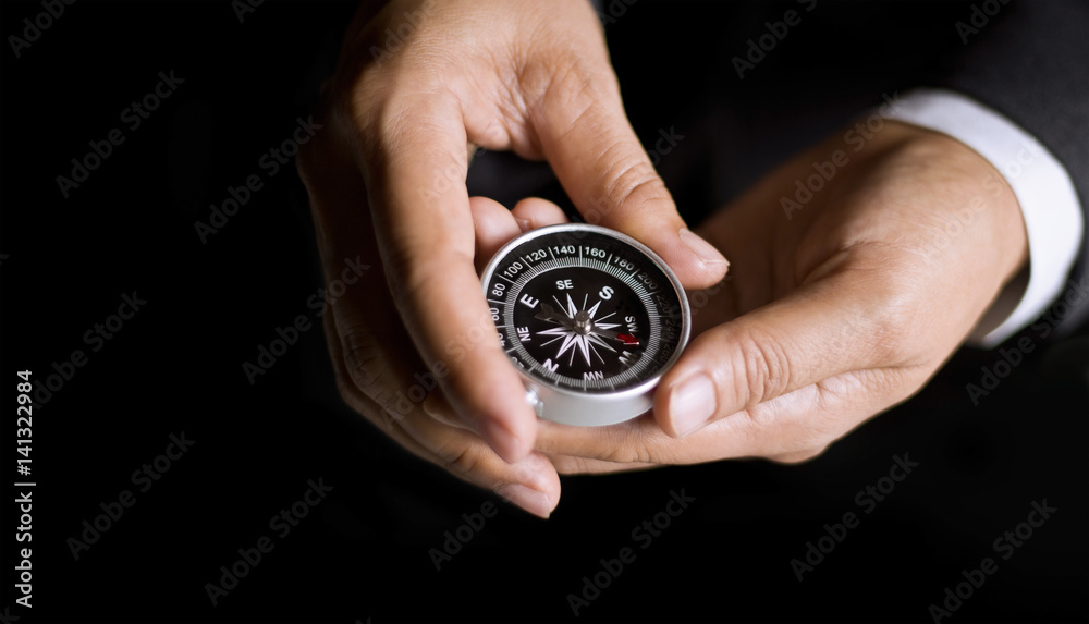 Businessman with a compass holding in hand on dark background Businessman with a compass holding in hand on dark background