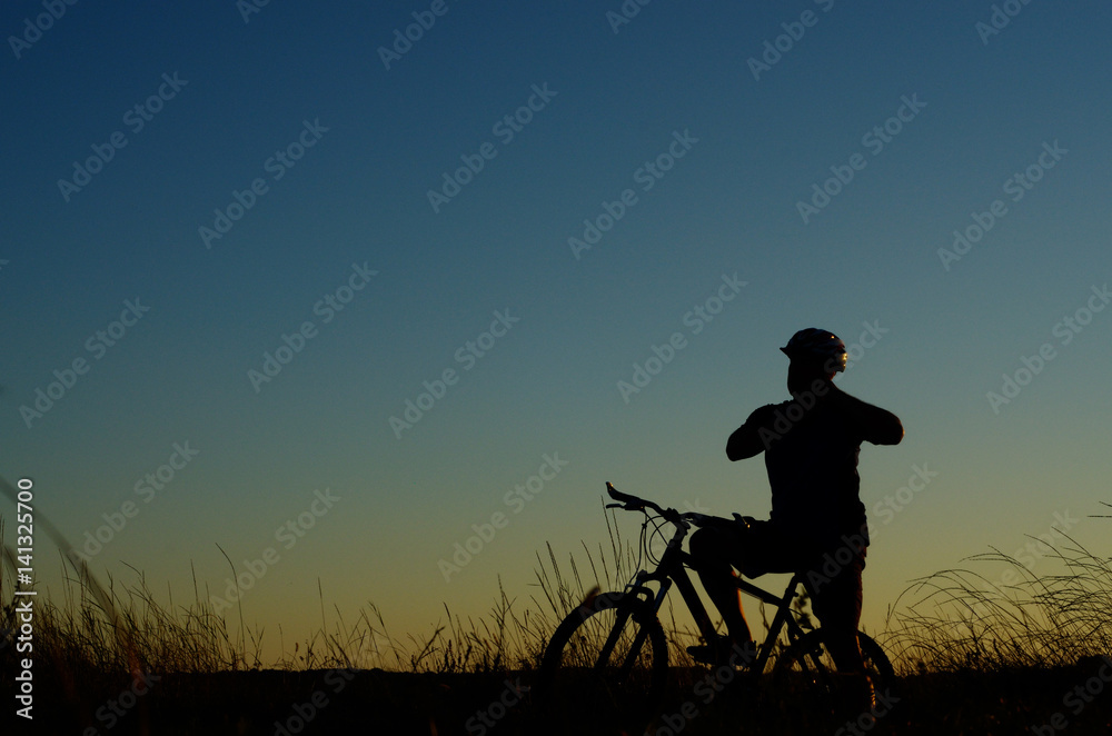 Adult cyclist silhouette having rest dusk time Adult cyclist silhouette having rest dusk time