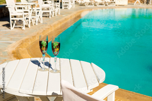 Two glasses with wine on a white table near the pool. Holiday season  It s time to travel. loving couple together on a tropical island. Concept of leisure and travel. Vacation time