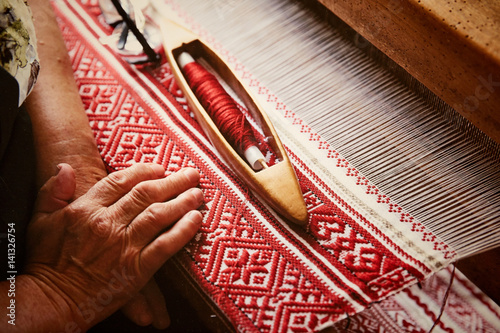An elderly woman weaves fiber from Belarusian patterns