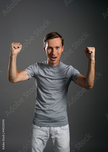 Gesture of success. Smiling man in gray t-shirt with raised hands.