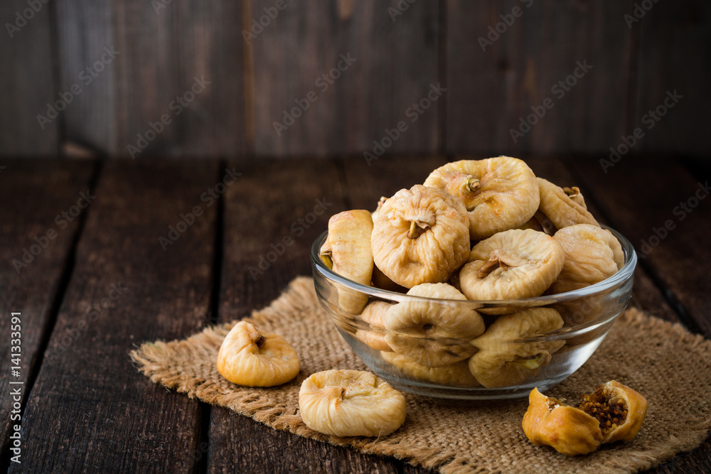 Dried figs in glass bowl on wooden background.