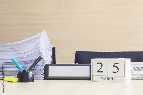 Closeup white wooden calendar with black 25 march word on blurred brown wood desk and wood wall textured background in office room view with copy space , selective focus at the calendar