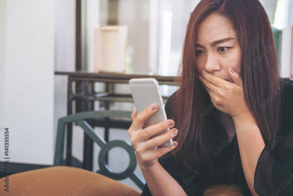 A beautiful asian woman looking at smart phone with feeling frightened in modern cafe A beautiful asian woman looking at smart phone with feeling frightened in modern cafe