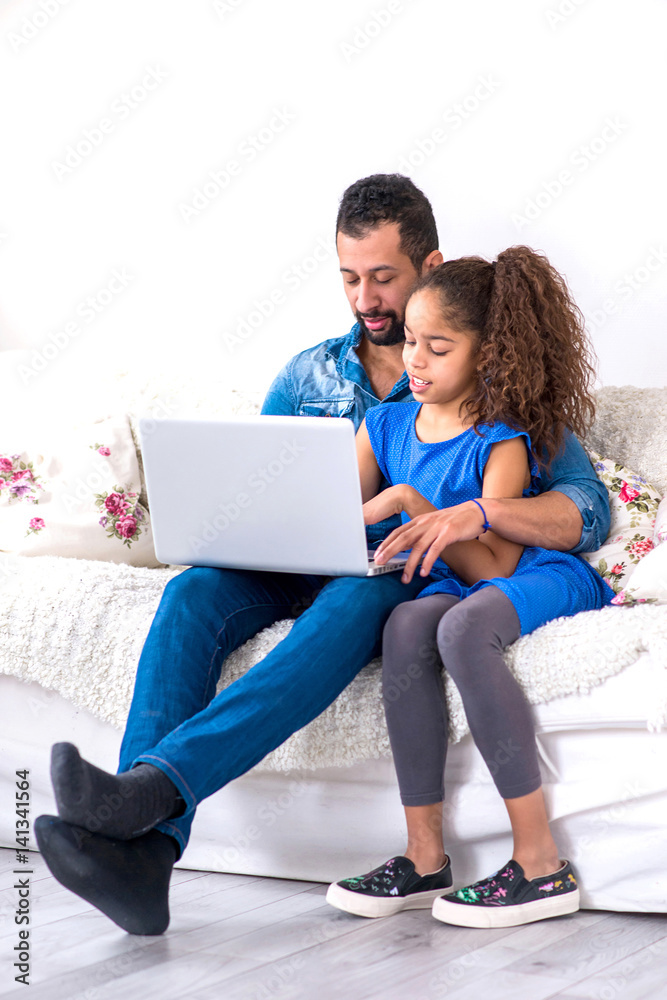 Black father and his daughter siting on a couch with a laptop