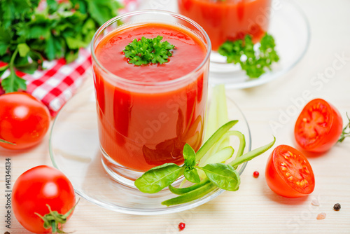 tomato juice in transparent glasses with parsley and cucumber on table, close up