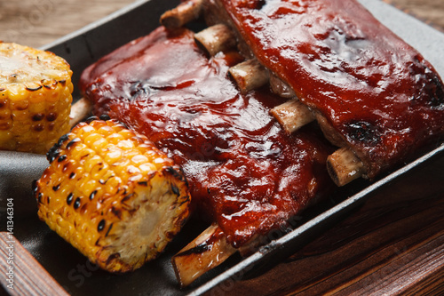 American delicious food. Appetizing grilled pork ribs with corn served on shovel, close up view. Junk food, picnic, bbq concept