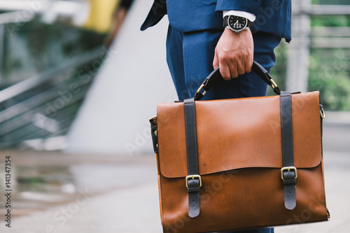 Closeup Of A Businessman wear the watch and Holding leather Briefcase Going To Work with the sunshine photo