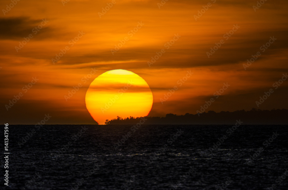 The sun setting over the island on the horizon at the ocean.