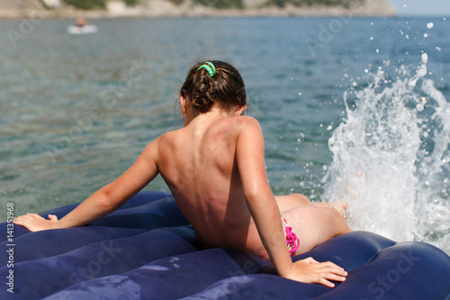 The girl on the air mattress swims on the sea and makes splashes on the water with her feet. Summer, sun, vacation. photo