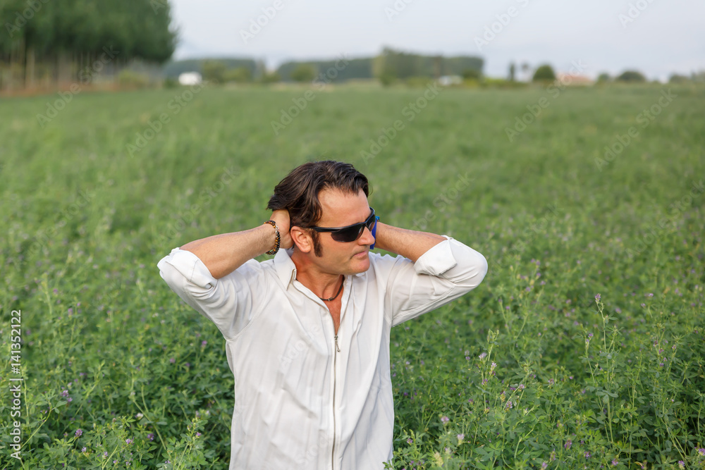 Man with sunglasses gathers his long hair while in the middle of nature Man with sunglasses gathers his long hair while in the middle of nature