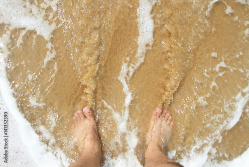 Top view of a man's leg standing on the sand and lapped by the ocean waves