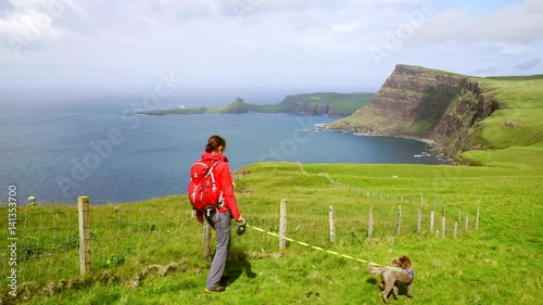 Hiker and their dog walking along the steep cliffs over Oisgill Bay towards Neist Point near Dunvegan on the Isle of Skye, Scotland. UK. photo