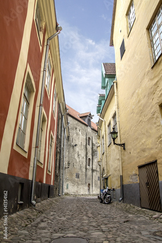 Narrow paved  stone  street in Tallinn between high houses.  motorcycle costs at  house wall