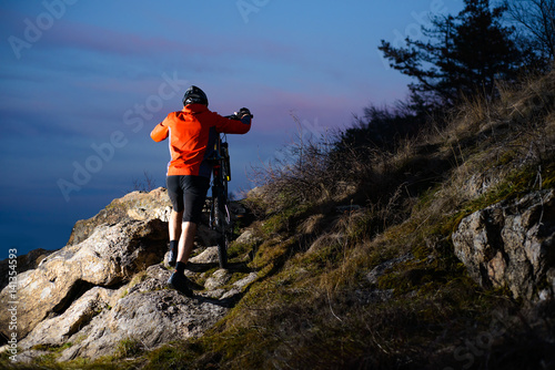 Enduro Cyclist Taking his Bike up the Rocky Trail at Night. Extreme Sport Concept. Space for Text.