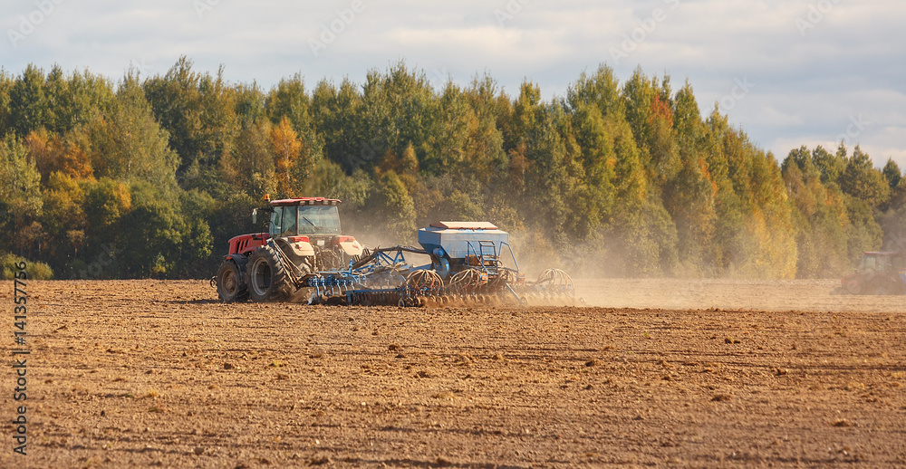 Fototapeta premium Sowing of crops on the field. Two tractors cultivate the soil on the field.