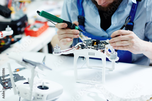Closeup shot of unrecognizable man  testing electric current in circuit board of disassembled drone using multimeter tool on table in maintenance shop