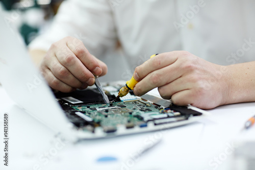 Closeup shot of male hands working on disassembled laptop with screwdriver and tweezers looking for broken pats