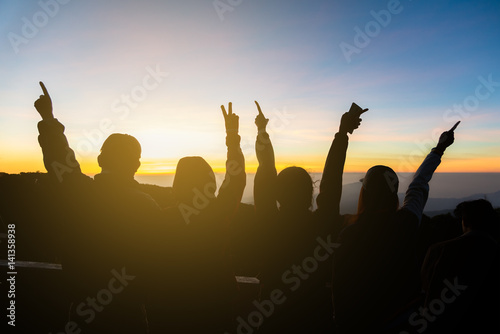 Silhouette of happy people raising their hands with a sun background.