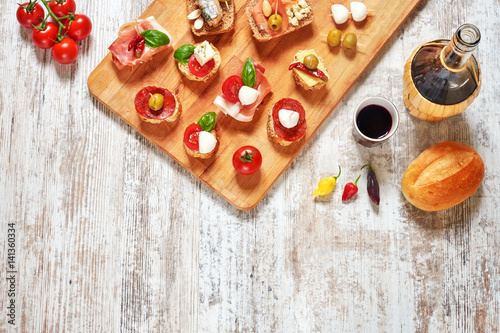 Mix of appetizers / snacks. Mediterranean tapas or antipasti on a rustic wooden table. Sandwiches with salami, jamon, sardines, salmon, cheese, tomato, olives, pepper, basil. Red wine. Copy space.