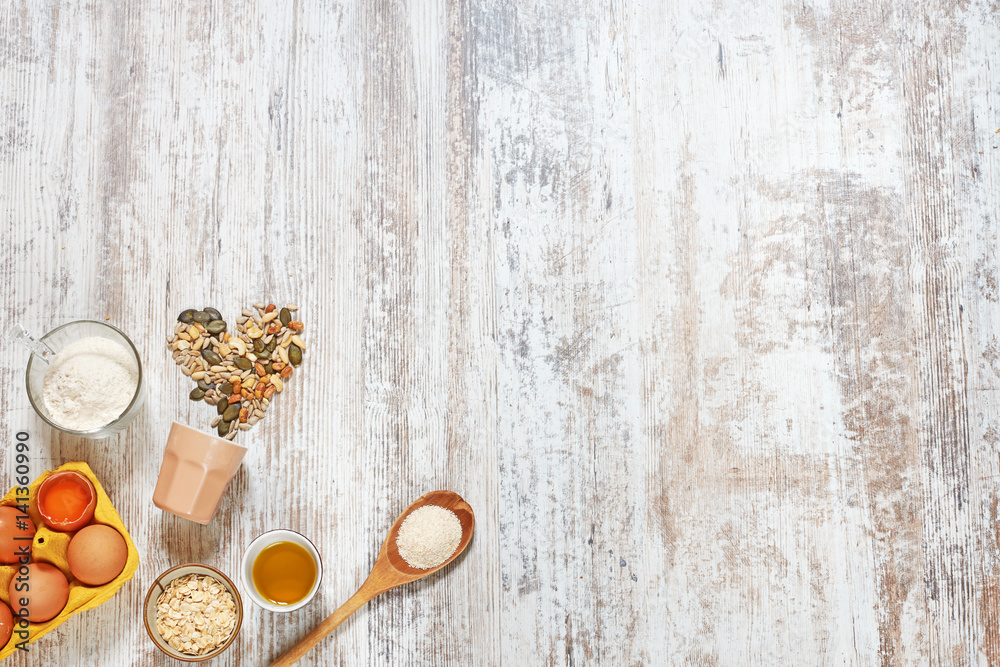Baking background. Wholegrain flour, eggs in a carton tray, olive oil, grains and seeds, oat flakes, wooden spoon on a light rustic table. Space for text. Baking background. Wholegrain flour, eggs in a carton tray, olive oil, grains and seeds, oat flakes, wooden spoon on a light rustic table. Space for text.