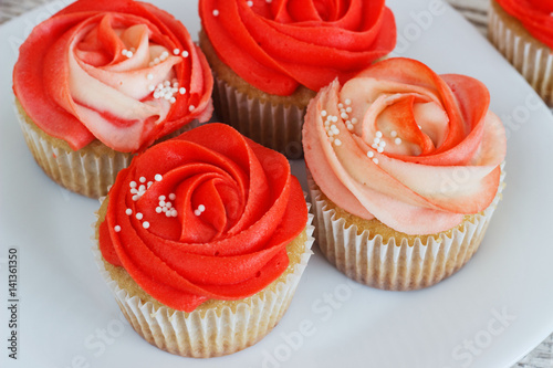 Vanilla cupcakes decorated with a red rose from a cream on a white background