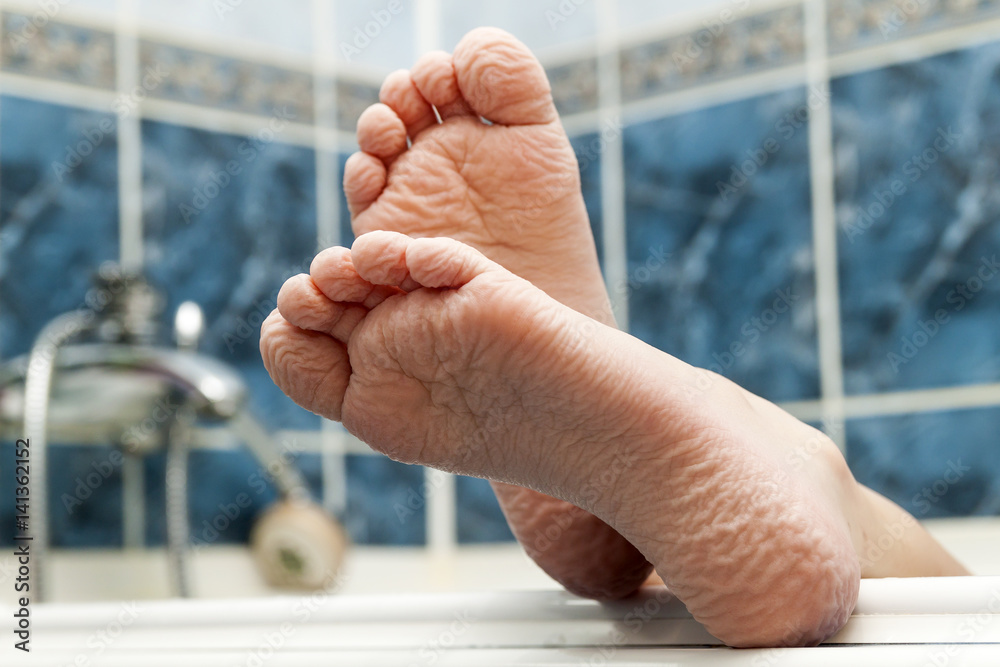 Wrinkled bare feet coming out from a bathtub. Young person getting a bath feet closeup indoor