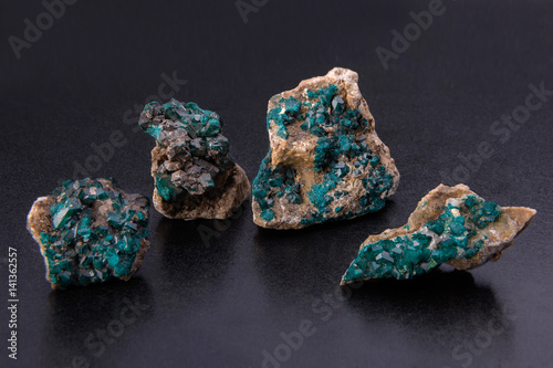 four minerals dioptase, green transparent crystals on a stone, against a dark background