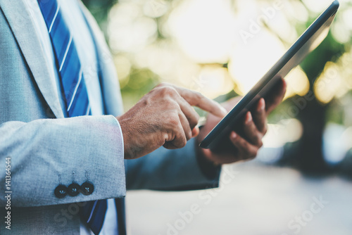 Closeup image of male hands using modern digital tablet device outdoors, professional businessman typing text information in internet during a break, manager using tablet pc to analyzing market