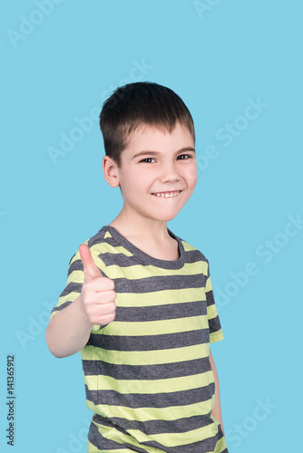 portrait of happy smiling teenage boy showing thumbs up gesture, isolated over blue background