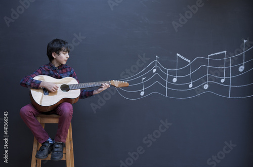 Boy playing guitar in front of chalkboard wall with showing musical notation