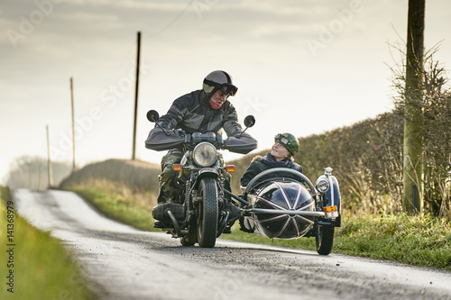 Senior man and grandson riding motorcycle and sidecar along rural road