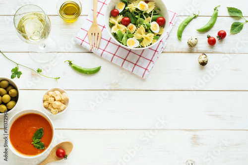 Light summer dinner / supper concept. Green salad with pasta, cherry tomato, quail eggs, olive oil. Cold tomato soup (gazpacho), croutons, green olives and glass of cold white wine. 
