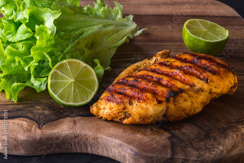 Grilled chicken breast served with green fresh salad, lime and chili sause on wooden cutting board