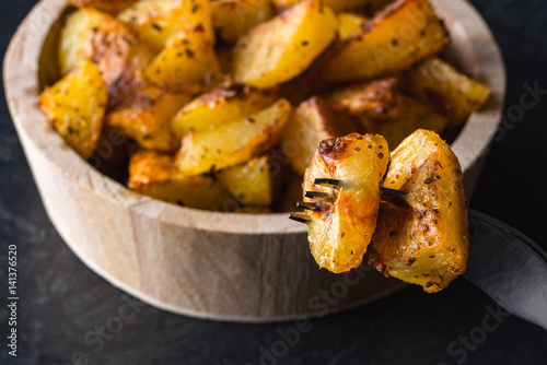 Roasted or backed potatoes in wooden bowl on black background