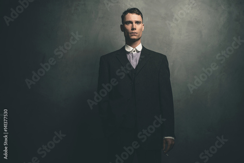 Retro 1920s english gangster in suit standing with cigarette.